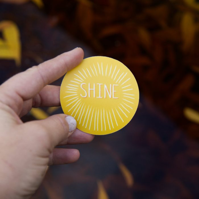 round sticker with yellow background and the word shine in the center